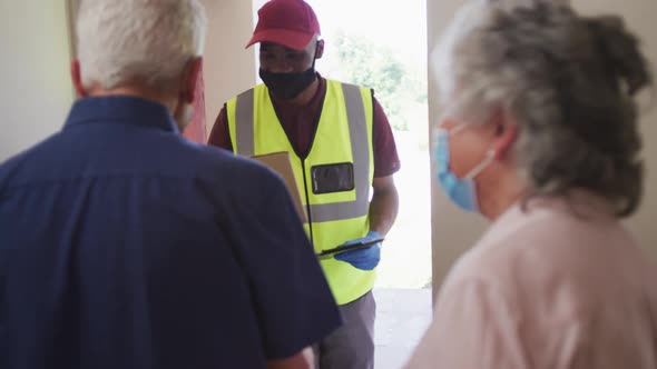 Senior caucasian couple wearing face masks standing by front door to delivery man in face mask