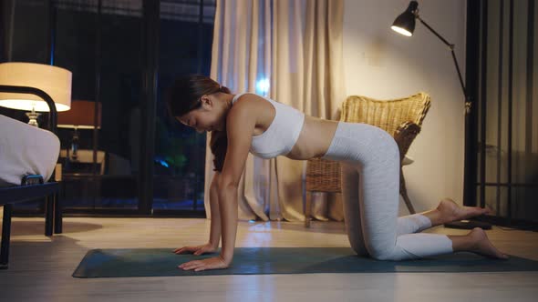 Young Asian lady in sportswear doing yoga exercise working out in living room at home at night.