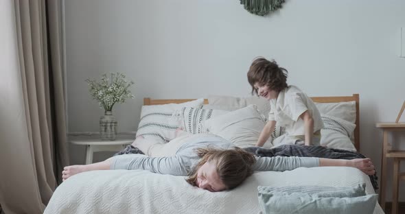 Laughing Young Mom Fooling Playing with Cute Child Son Lying Jumping on Comfy Bed at Bedroom