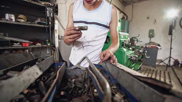 Teen Boy Looking Inside Rusty Toolbox and Searching for Detail While Working in Workshop