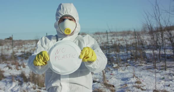 Virologist in Protective Suit Hold Plastic Plate with Inscription "Stop Plastic"