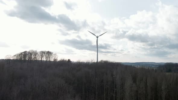 Wind turbine spinning fast behind a dark, dry forest in western Germany. Aerial ascending tracking s