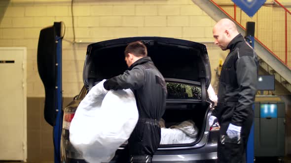 Mechanics Taking Tires Out of Car Trunk at Service