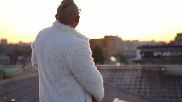 Carefree Adult Man Dancing at Sunset on Roof in Urban City Drinking Wine From Bottle