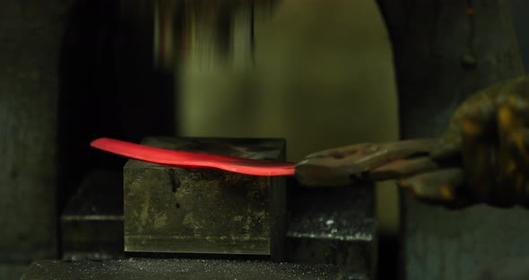 Bladesmith working with hot blade at hydraulic forge hammer