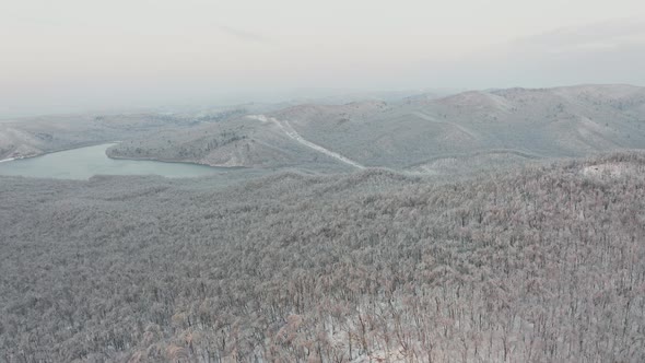Drone Flight Over a Winter Forest and a Highway Among the Hills in the Evening