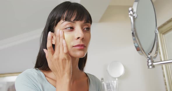 Caucasian woman looking in mirror and using cream on face in bathroom