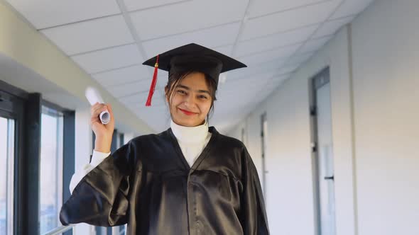 Pakistani Female Graduate in Mantle Stands with a Diploma in Her Hands and Smiles