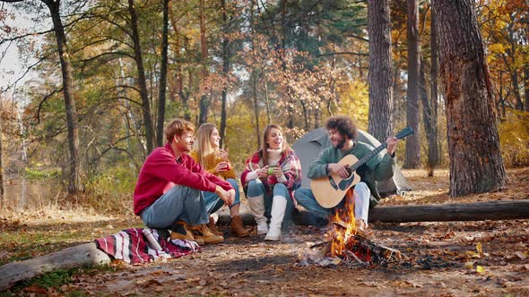 Young Males and Females Smiling Playing Guitar Listening to Music and Singing Songs While Sitting on