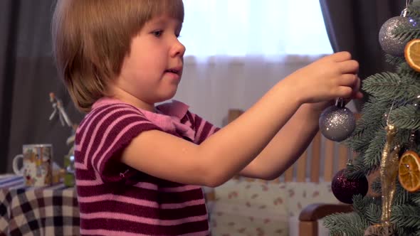 Little Girl in Beautiful Dress Decorates the Christmas Tree