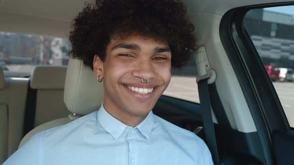 Close Up Young African American Guy in Shirt Sitting in Modern Car Interior Looking at Camera and
