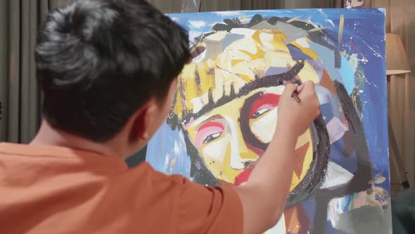 Hind View Of An Asian Artist Boy In Wheelchair Painting A Girl's Face On The Canvas