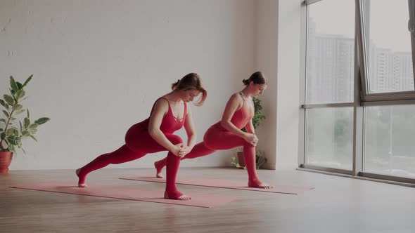 Two Women in Red Sports Uniforms Make Virabhadrasana in Yoga Studio