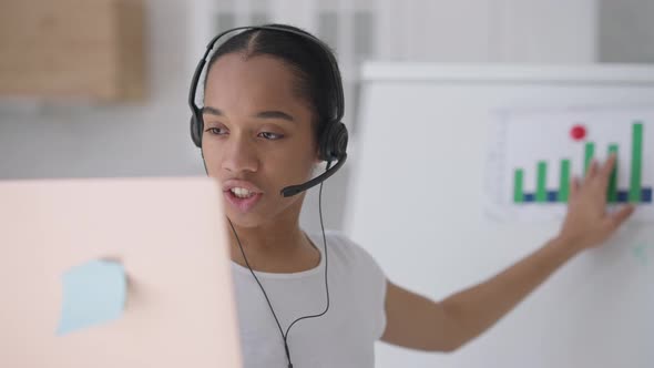 Portrait of Serious Beautiful Confident African American Woman in Earphones Talking at Laptop in