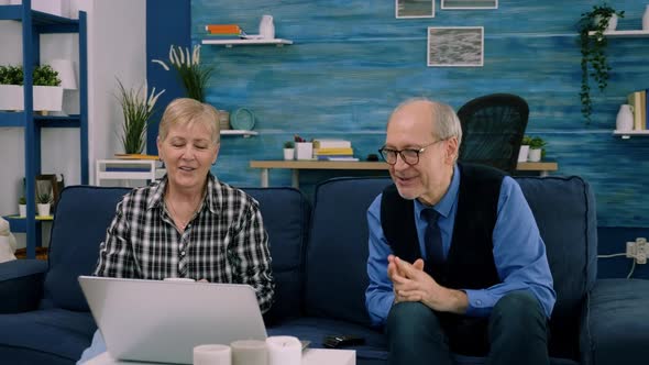 Elderly Age Couple Sitting on Sofa Waving at Camera During Videocall