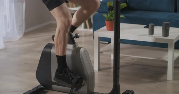 Training with Stationary Bicycle at Home Closeup View of Legs of Middle Aged Man Spinning Pedals