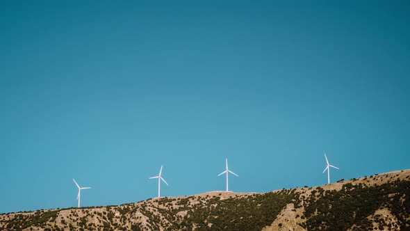  Time Lapse of Wind Mill Turbines on Top of Mountain Range Against Bright Blue Sky