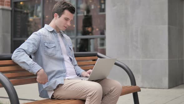 Young Man with Back Pain Working on Laptop Outdoor