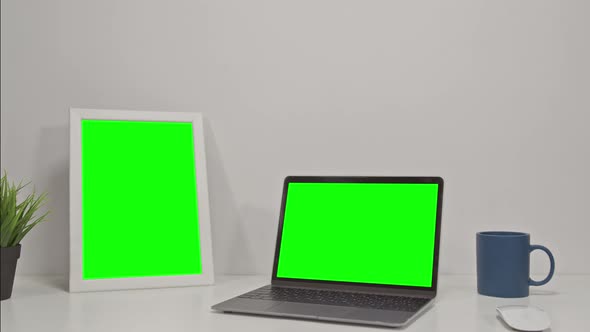 Two Elecronic Devices Laptop Computer and Tablet with Green Screen on a White Office Desk