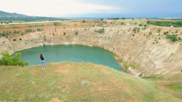 Fit Girl in Jeans Sitting on the Edge of an Abandoned Open Mine Pit