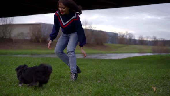 A Dark-haired, Cheerful, Pretty Girl with Bright Red Lipstick Runs Across the Grass After a Small