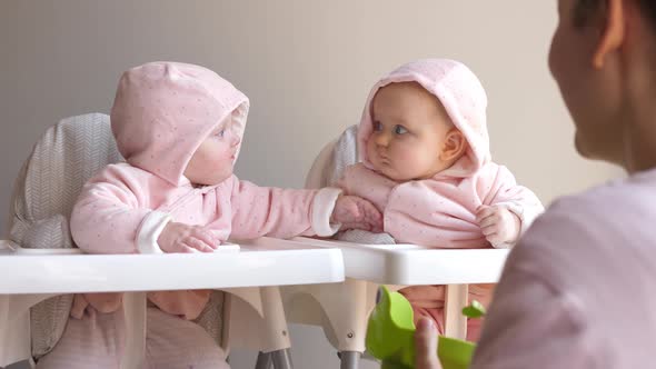 Young Mother Feeding Her Twin Babies Sitting On Hair Chairs. Baby Food Concept. 