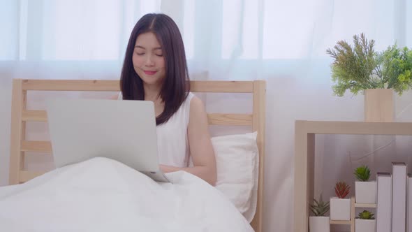 Young business freelance Asian woman working on laptop checking social media while lying on the bed.