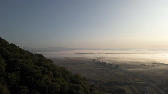 Mist covering vast flat landscape. Tree covered hill being revealed.