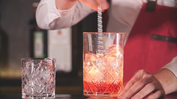 Bartender Using Long Metal Spoon To Mix Ice Cubes with Drink in a Glass