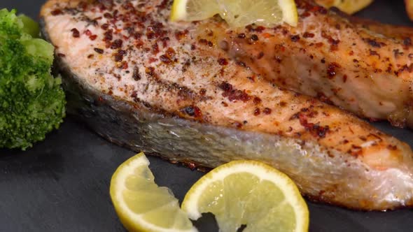 Baking salmon fillets spinning on a black plate with lemon slice, french fries and boiled broccoli