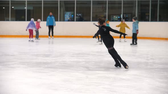 A Girl Figure Skater in Black Costume Training Her Skating on the Public Ice Rink