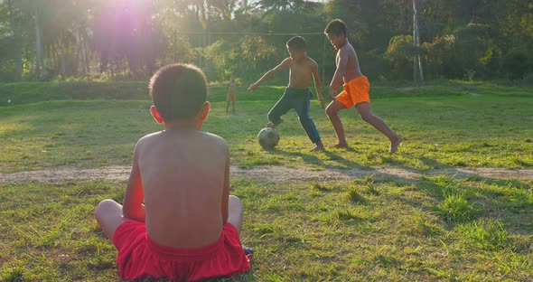 Rural Boy Sitting And Watching Friends Playing Soccer