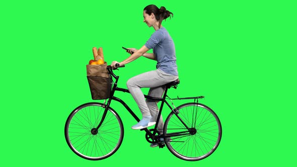 Casual Woman Riding a Bicycle Over a Green Screen While Texting or Using an App