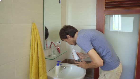 A Young Man Uses a Portable Water Flosser Dental Oral Irrigator To Clean His Teeth