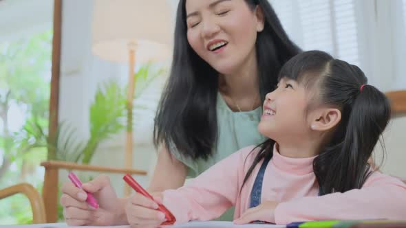 Asian loving parent mother with small little kid daughter having fun drawing and coloring picture