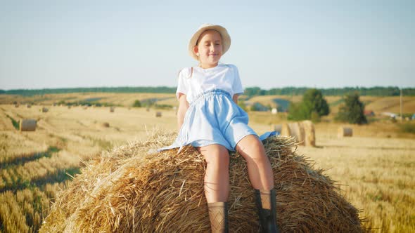 Pretty Girl in Blue Dress Walks in a Field with Haystacks