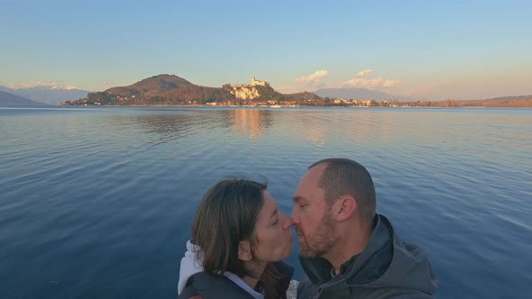 Couple in love kiss with lake and Angera castle in background at sunset, Italy