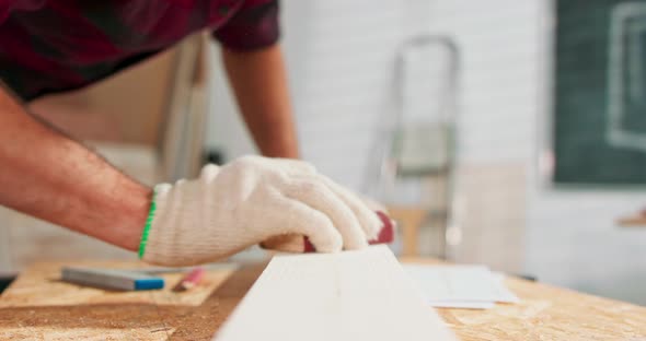 A Bearded Handyman is Sanding Wood for Furniture in a Carpentry Workshop The Carpenter Blows Off the