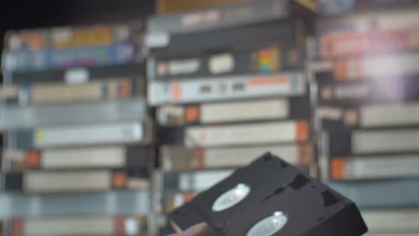 Male Hand Picks Up a VHS Cassette From the Shelf.