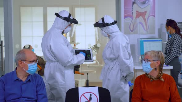 Man Discussing with Nurse in Dental Reception Wearing Protection Suit