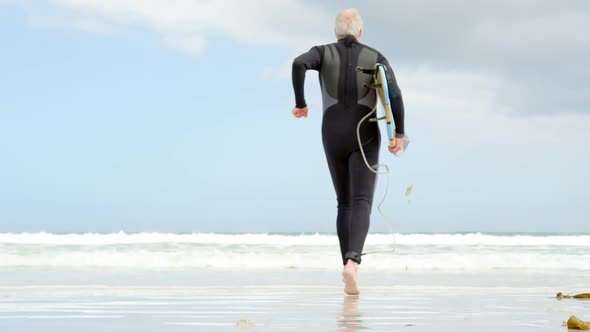 Rear view of old caucasian senior man running with surfboard at beach 4k