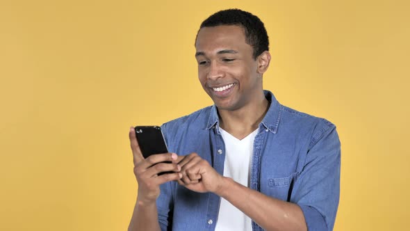 Young African Man Browsing Smartphone, Yellow Background