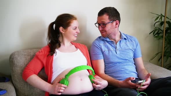 Pregnant woman placing headphones while interacting with man