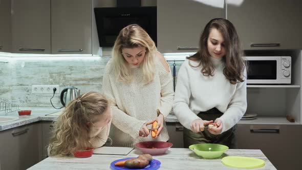 Young Mother and Two Her Daughters Cooks Salad at Kitchen