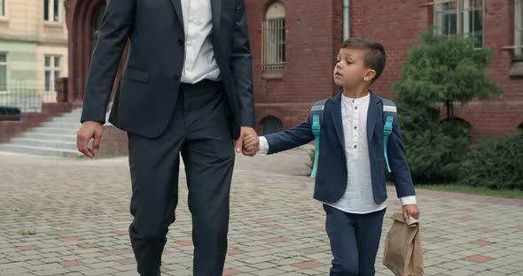 Crop View of Litlle Boy with Bag and His Father in Suit Holding Hand in Hand. Father with Little Kid