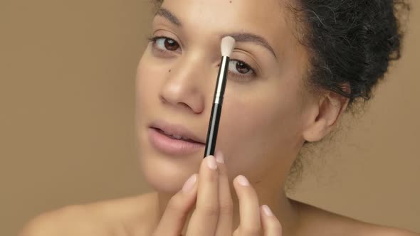 Beauty Portrait of Young African American Woman Looking in Mirror and Doing Eye Makeup Using Brush