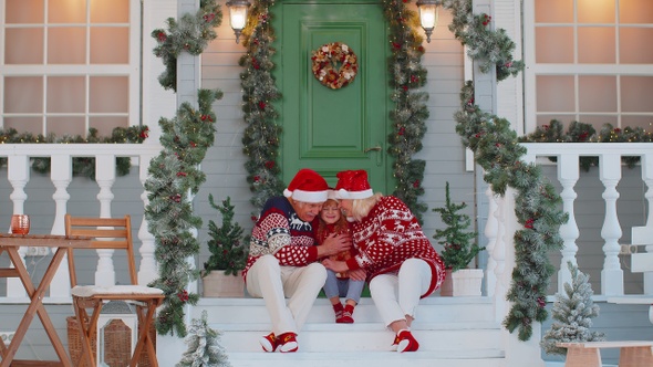 Senior Grandparents Near Decorated Christmas House Celebrating Together with Granddaughter at Home