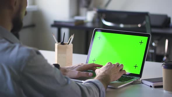 Man Working on Laptop with Green Screen at Office