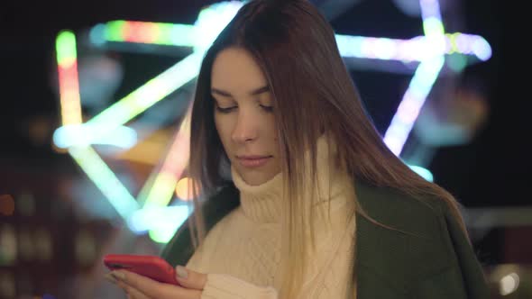 Portrait of Cute Caucasian Girl in White Sweater Using Smartphone and Smiling. Beautiful Girl