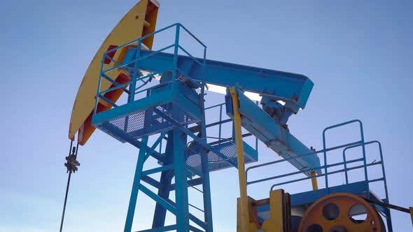 Industrial Equipment Is Pumping Petroleum and Natural Gas From Ground, Tilt Up View Against Blue Sky
